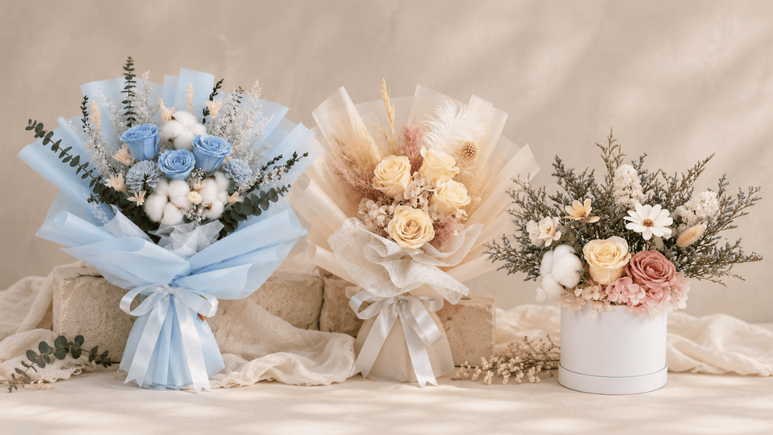 Three preserved flower arrangements against a soft beige backdrop: blue and cream bouquets with a pastel flower box.