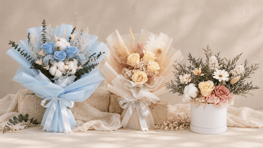 Three preserved flower arrangements against a soft beige backdrop: blue and cream bouquets with a pastel flower box.